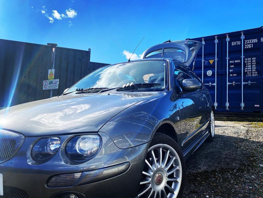a large motor car parked in front of a row of storage shipping containers