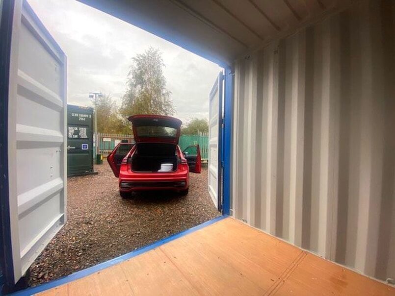 A van at a storage facility beside a row of shipping containers used for storage purposes