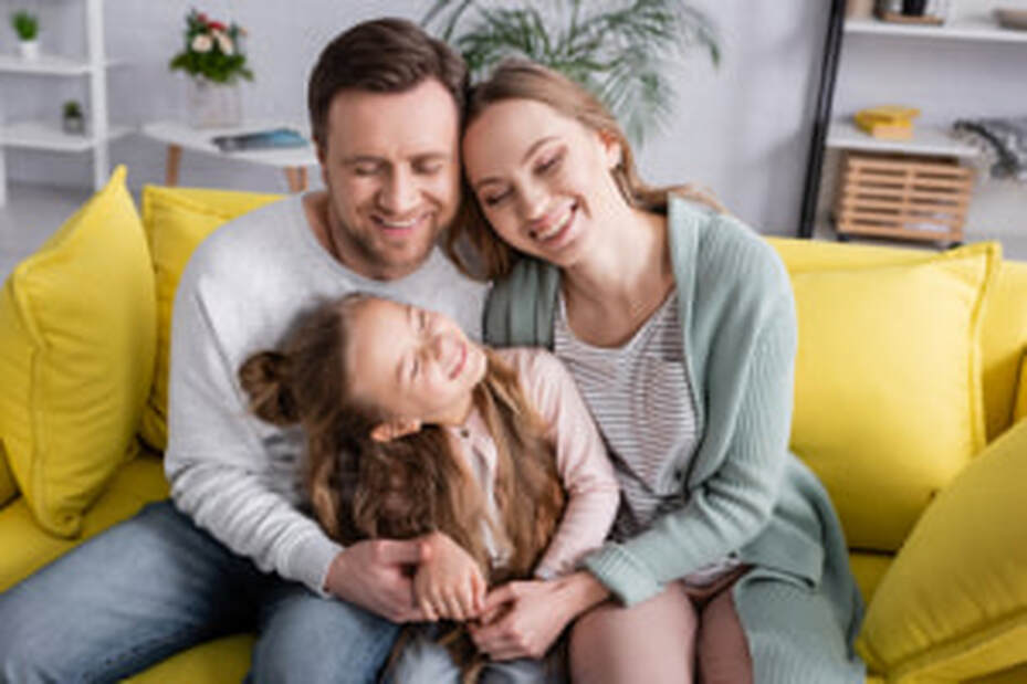 mother, father and daughter happy sat on a sofa