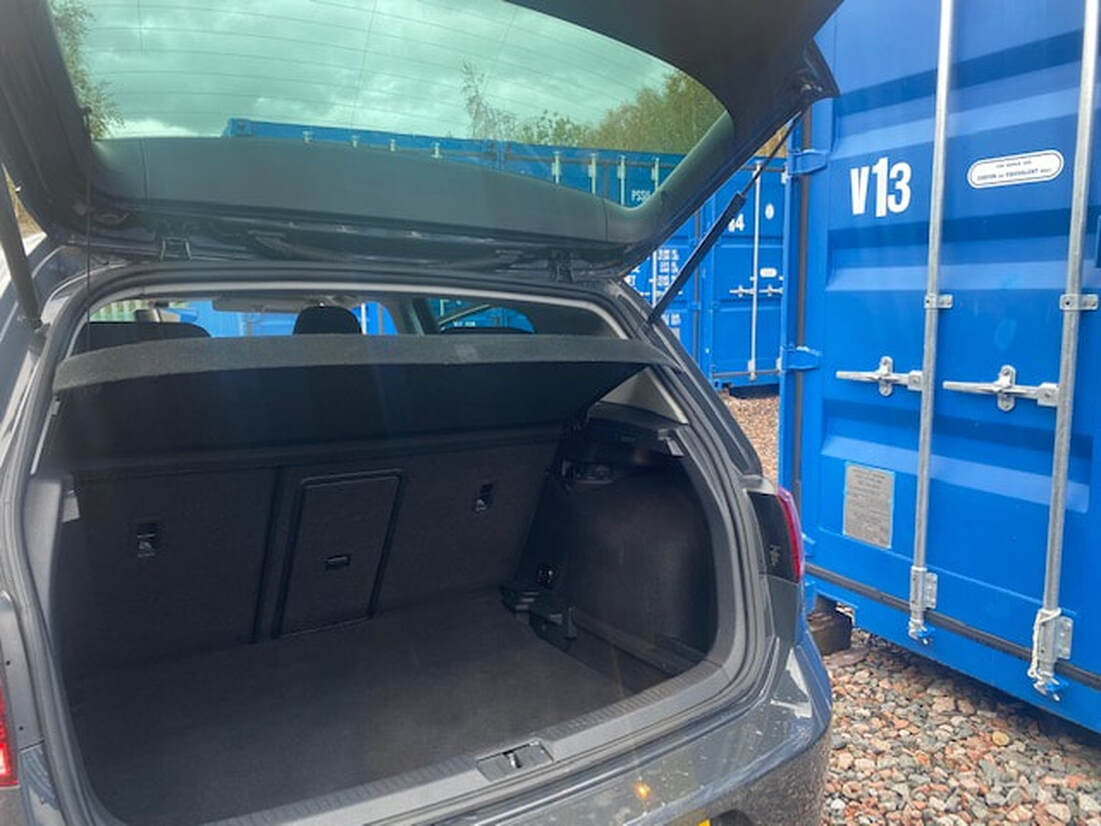 car with rear boot wide open parked next to a shipping container on a storage facility